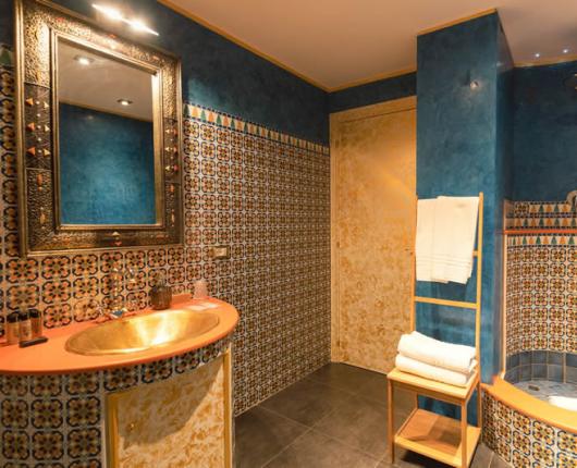 Bathroom with a golden sink and a shower decorated with colorful tiles.