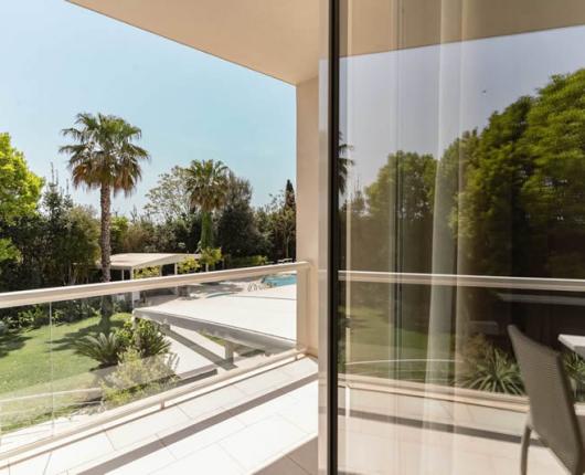 Balcone con vista su giardino e piscina, circondato da palme.