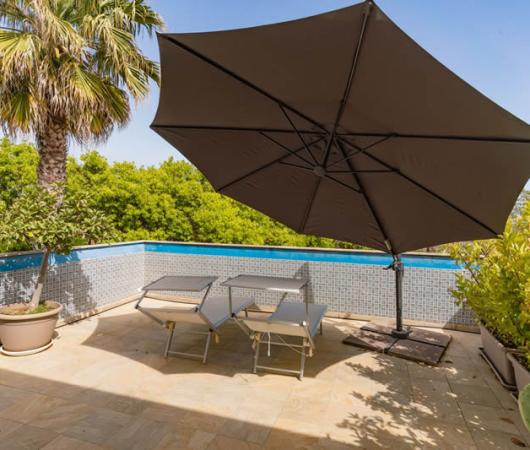 Terrace with umbrella, lounge chairs, and pool, surrounded by plants.