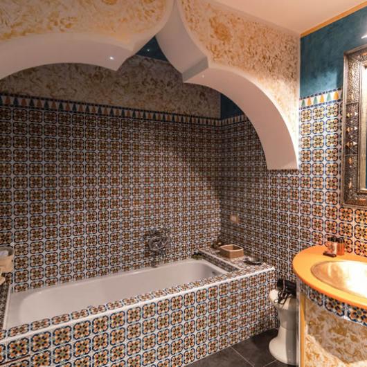 Bathroom decorated with colorful tiles, bathtub, and golden sink.