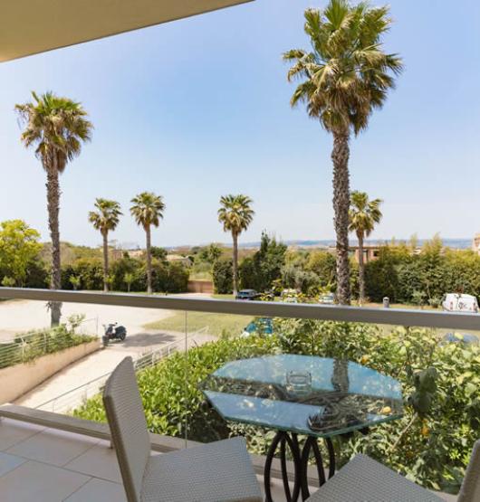 Balcone con vista su palme e mare, tavolo con sedie.