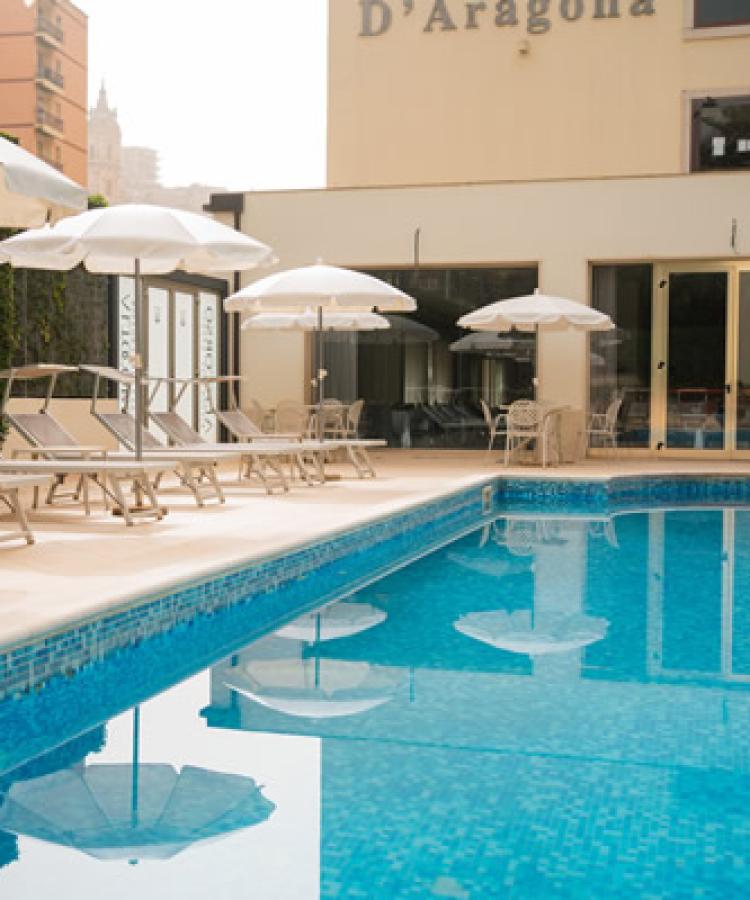 Outdoor pool with white loungers and umbrellas, surrounded by buildings.