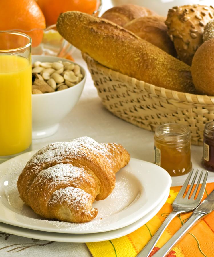 Colazione con croissant, succo d'arancia, pane e marmellata.